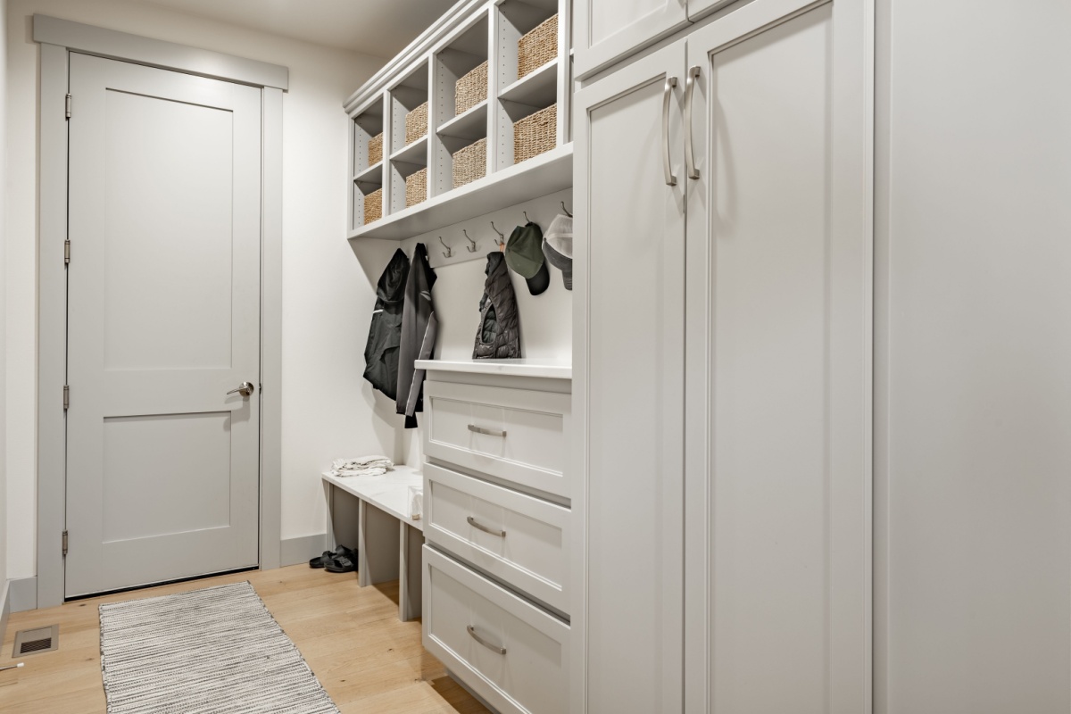 Mudroom with white cabinets and a bench that has coats hanging above it on hooks